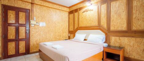 A hotel room with a wooden paneled wall, a large bed with white linens, a wooden nightstand, and a door with a lock.