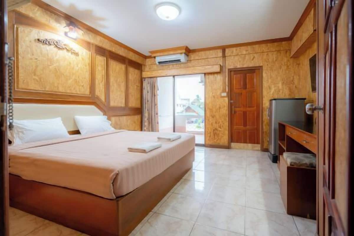 A hotel room with a bed, a TV, a wardrobe, and an air conditioning unit.