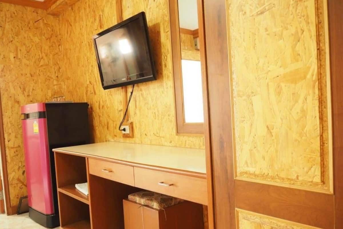 A room with a wooden paneled wall, a flat-screen TV mounted above a wooden desk with drawers, and a pink refrigerator.