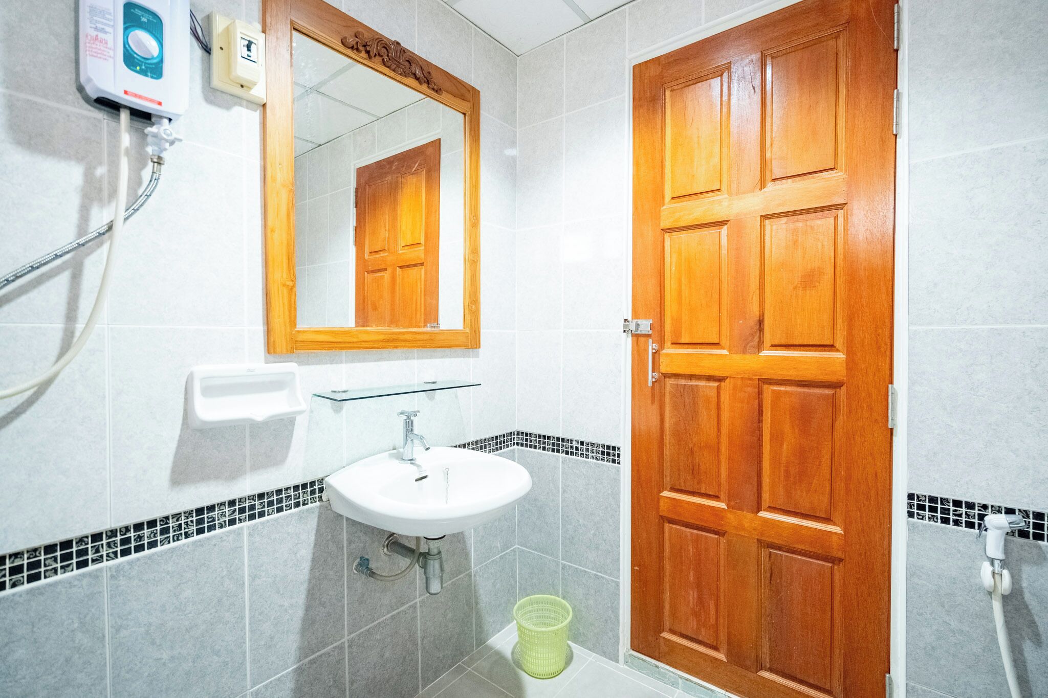 Un baño con puerta de madera, un lavamanos blanco, un espejo y un panel de control de ducha.