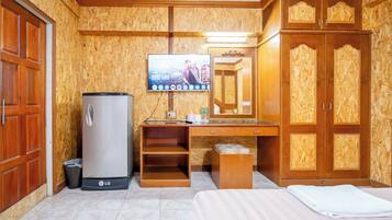 A hotel room with a wooden wardrobe, a desk with a flat-screen TV, a refrigerator, and a bed.