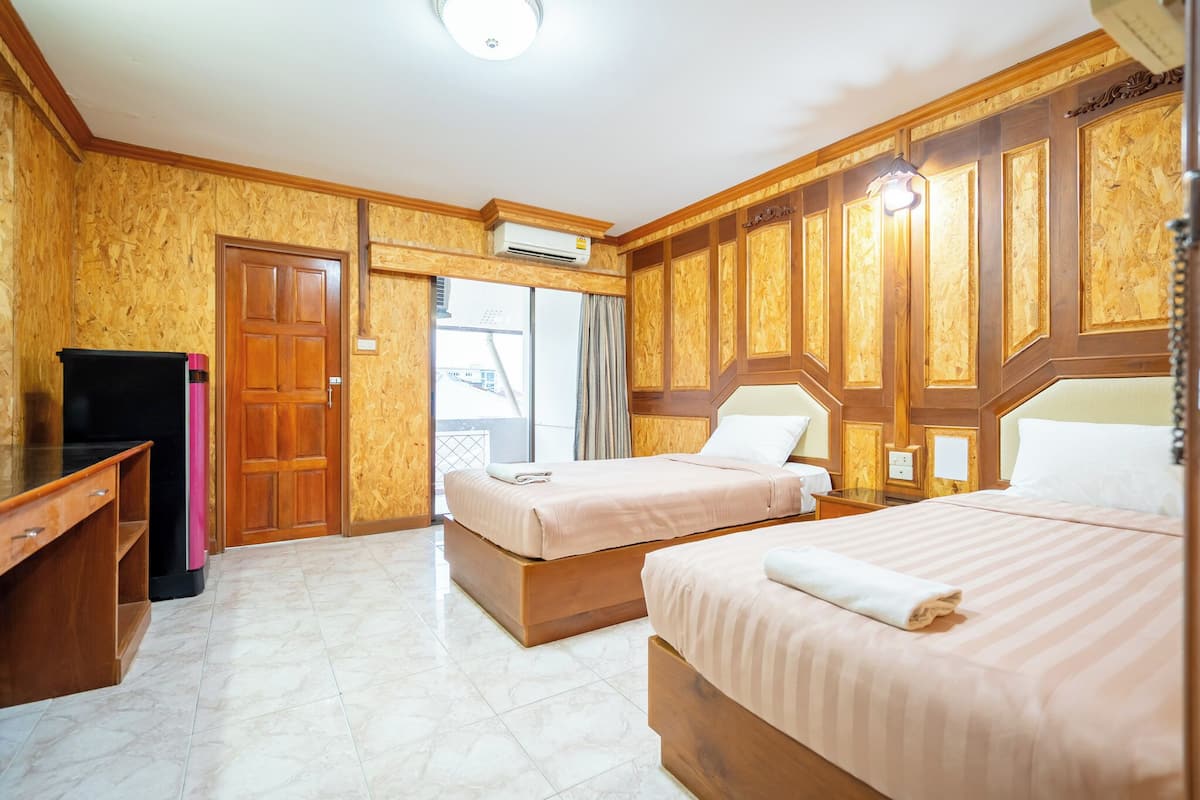 A hotel room with two beds, wooden paneling, a desk, and a sliding glass door to the balcony.