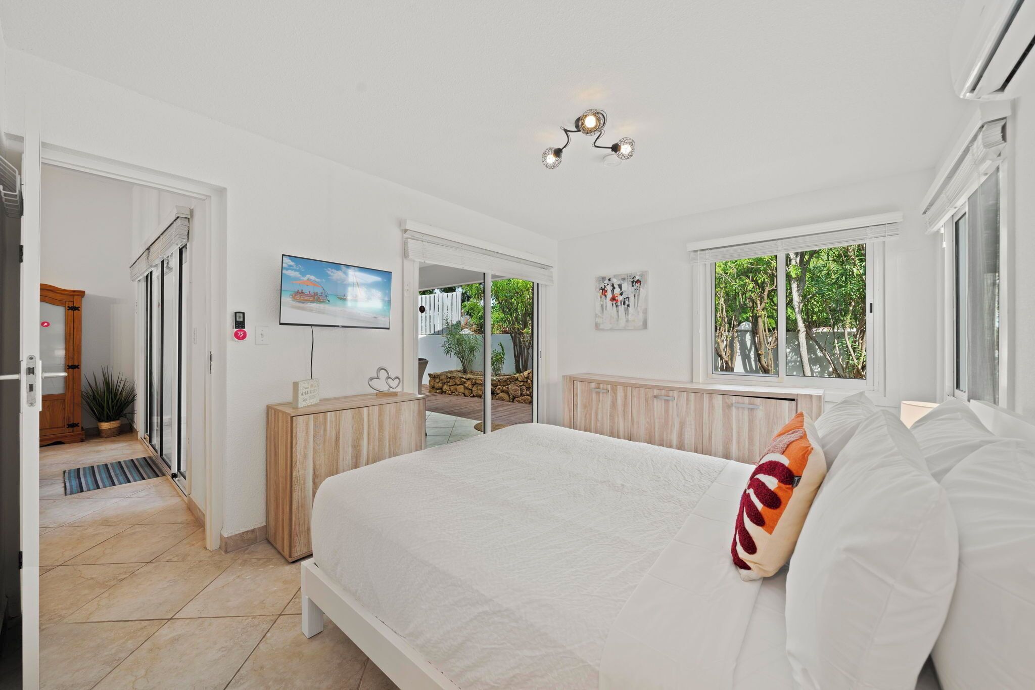 A modern bedroom with a large bed, a TV, and a view of the outdoors.