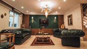 A living room with green paneled walls, a chandelier, leather sofas, a coffee table, and a television. - Samsun Charme Hotel (Samsun)