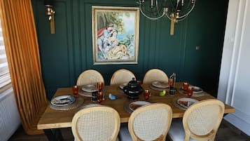 Comedor con mesa de madera dispuesta para seis comensales, rodeada de sillas de mimbre, un candelabro y un cuadro enmarcado en la pared.