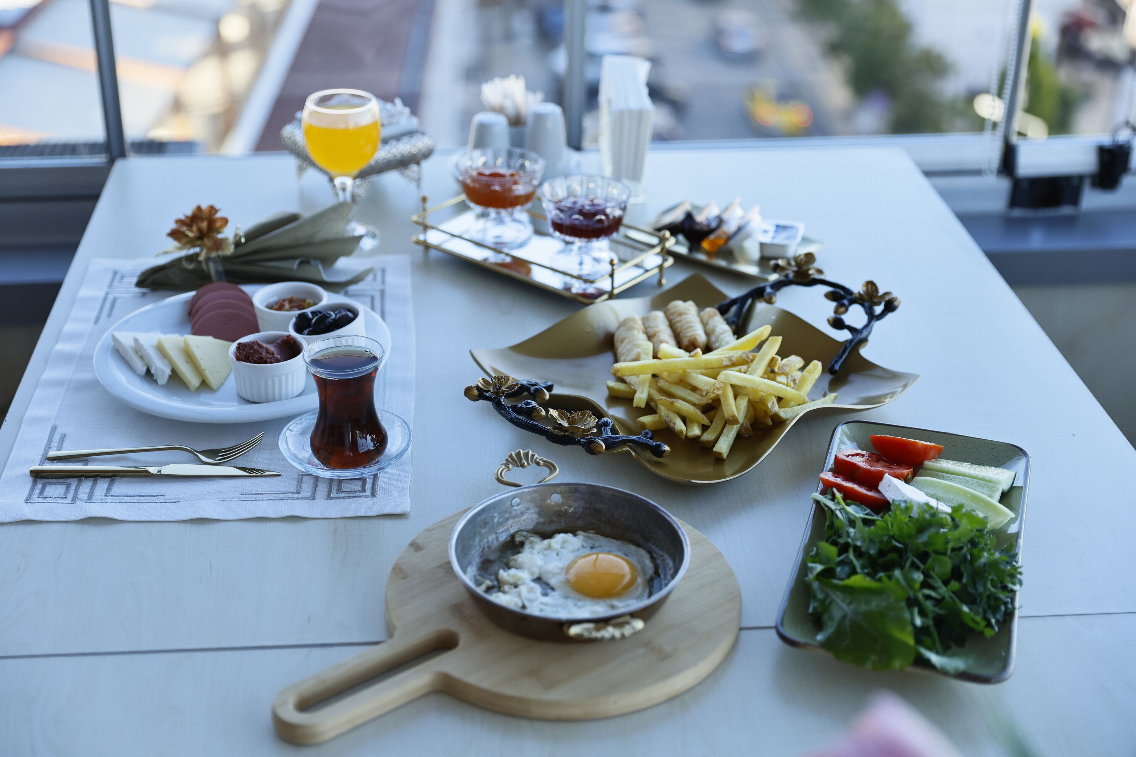 A table with a variety of food items including eggs, cheese, and salads, set on a white tablecloth with a view of the city through a window.