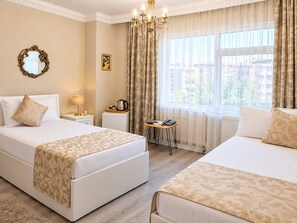 Une chambre d’hôtel avec deux lits, une table de chevet avec une lampe, une petite table avec une bouilloire et un téléphone, et une fenêtre avec des rideaux.