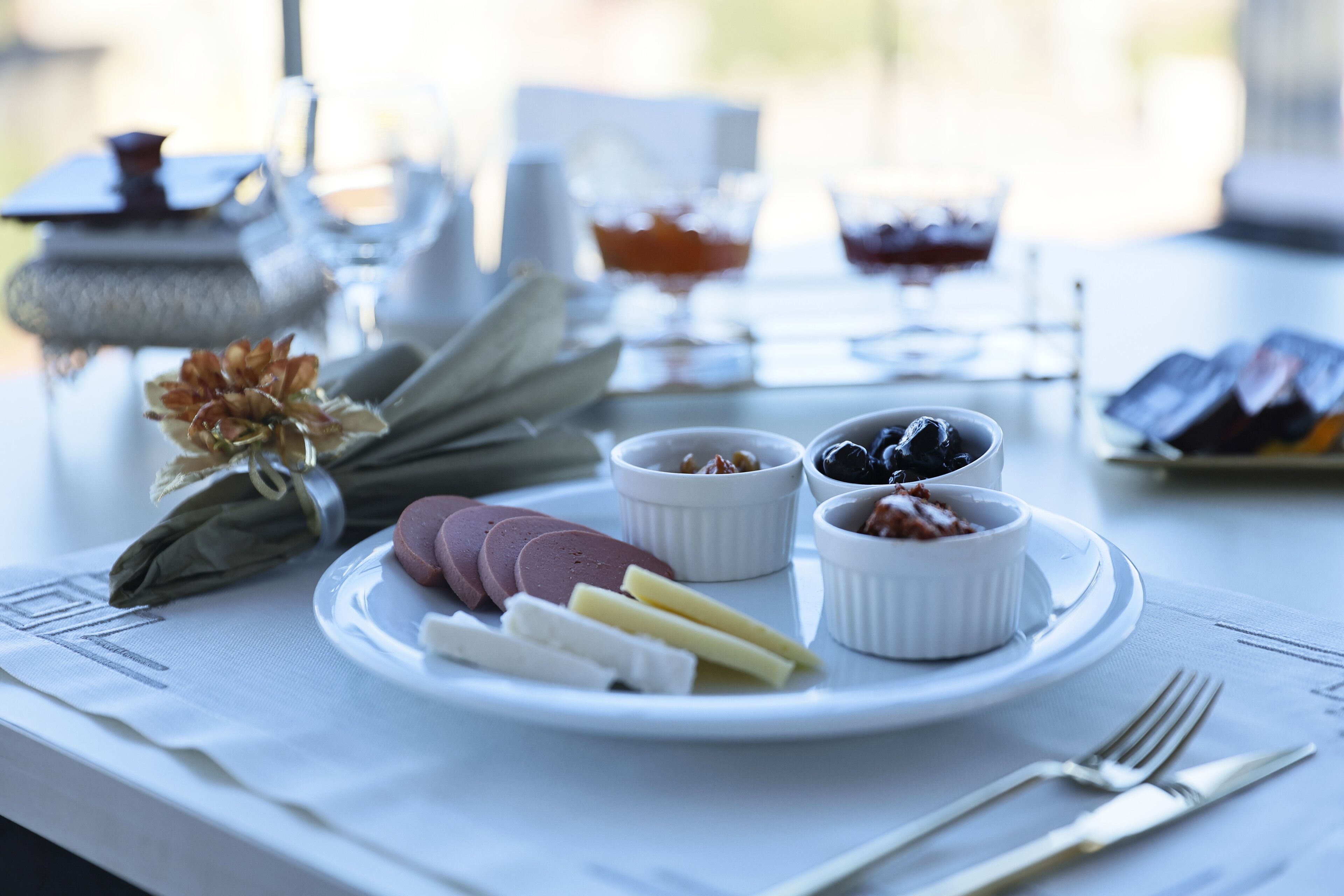 Una mesa con un plato de comida, que incluye carnes cortadas, quesos y aceitunas, junto con recipientes pequeños de salsas y aderezos.