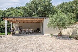 A covered patio area with a table and chairs, surrounded by potted plants and trees. - Relaxing Istrian Home with Pool, Garden, Barbecue – Family & Pet-Friendly (Bužinija)