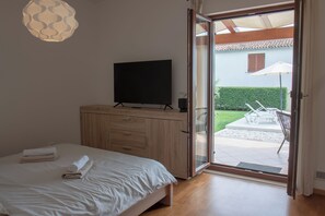 A bedroom with a bed, a TV on a wooden cabinet, and a sliding glass door leading to an outdoor patio with a table and chairs. - Relaxing Istrian Home with Pool, Garden, Barbecue – Family & Pet-Friendly (Bužinija)