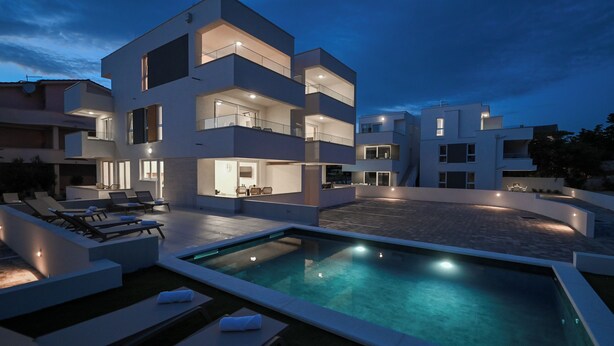 A modern multi-story building with a pool area, outdoor seating, and multiple balconies. - Two-bedroom apartment Break A1 next to the pool (Novalja)