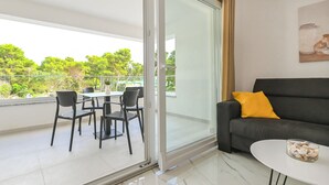 A modern living room with a glass door leading to a balcony, a black sofa with a yellow pillow, and a glass table with a bowl of shells. - Two-bedroom apartment Break A1 next to the pool (Novalja)