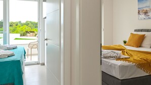 A hotel room with a bed, a table with towels, and a view of greenery outside. - Two-bedroom apartment Break A1 next to the pool (Novalja)