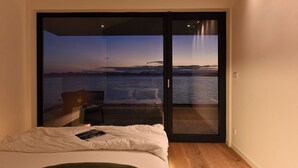 Un dormitorio con cama, mesita de noche y vistas al mar a través de un ventanal.