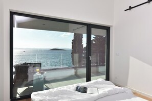 Un dormitorio con un gran ventanal corredera que da a un balcón con vistas al mar.