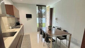 A modern kitchen with a built-in oven, a dining area with a table and chairs, and a large window providing a view of the outdoors. - Villa Branco in the North of Portugal (Barcelos)