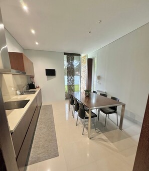 A modern kitchen with a built-in oven, a dining area with a table and chairs, and a large window providing a view of the outdoors. - Villa Branco in the North of Portugal (Barcelos)
