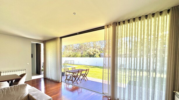 A spacious living room with a large sliding glass door leading to an outdoor area with a pool and garden. - Villa Branco in the North of Portugal (Barcelos)