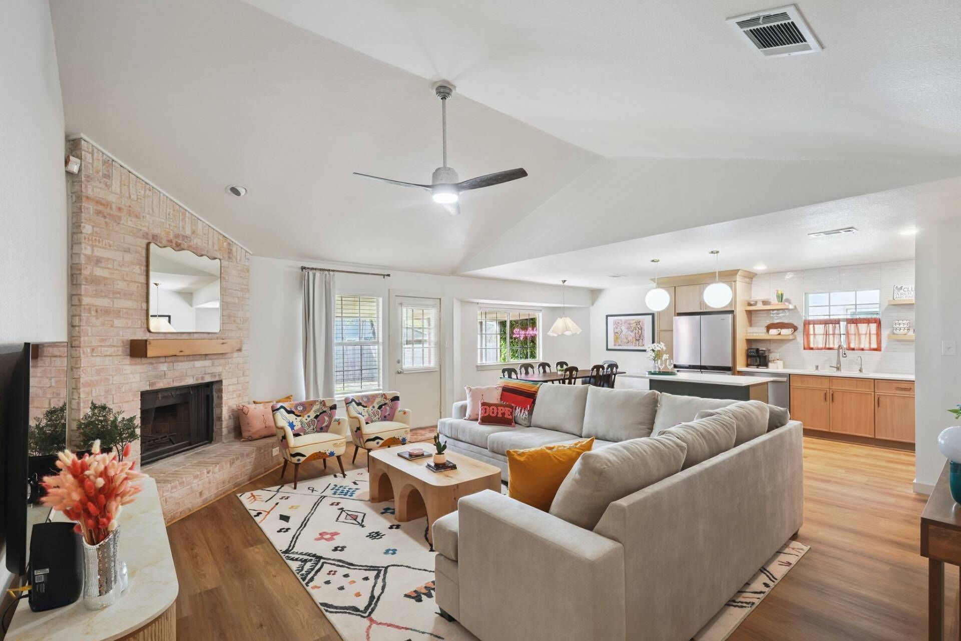 A spacious living area with a fireplace, a sofa, a dining table, and a kitchen in the background.
