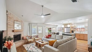 A spacious living area with a fireplace, a sofa, a dining table, and a kitchen in the background. - Newly Remodeled, Whimsical Retreat -  Viking Hot Tub, Ultimate Game Room, Massage Chair, BBQ (Round Rock)