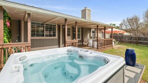 A hot tub with a wooden deck and a covered patio area. - Newly Remodeled, Whimsical Retreat -  Viking Hot Tub, Ultimate Game Room, Massage Chair, BBQ (Round Rock)