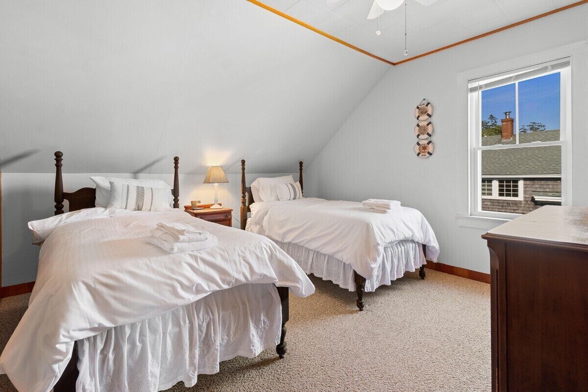 Una camera da letto con due letti, un comodino, una lampada, una cassettiera in legno e una finestra vista.