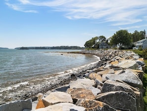 A rocky shoreline with a row of houses and a clear view of the water. - The Spruces: Classic 5BR ocean-views in Owls Head with deck, grill, and space for 10 (Owls Head)