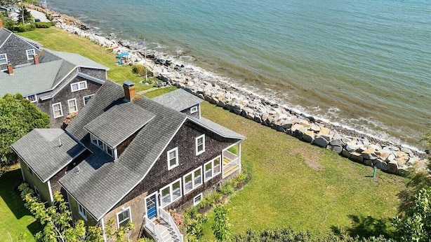 En ejendom ved kysten med et stort hus, en bro og en klippefyldt kystlinje.