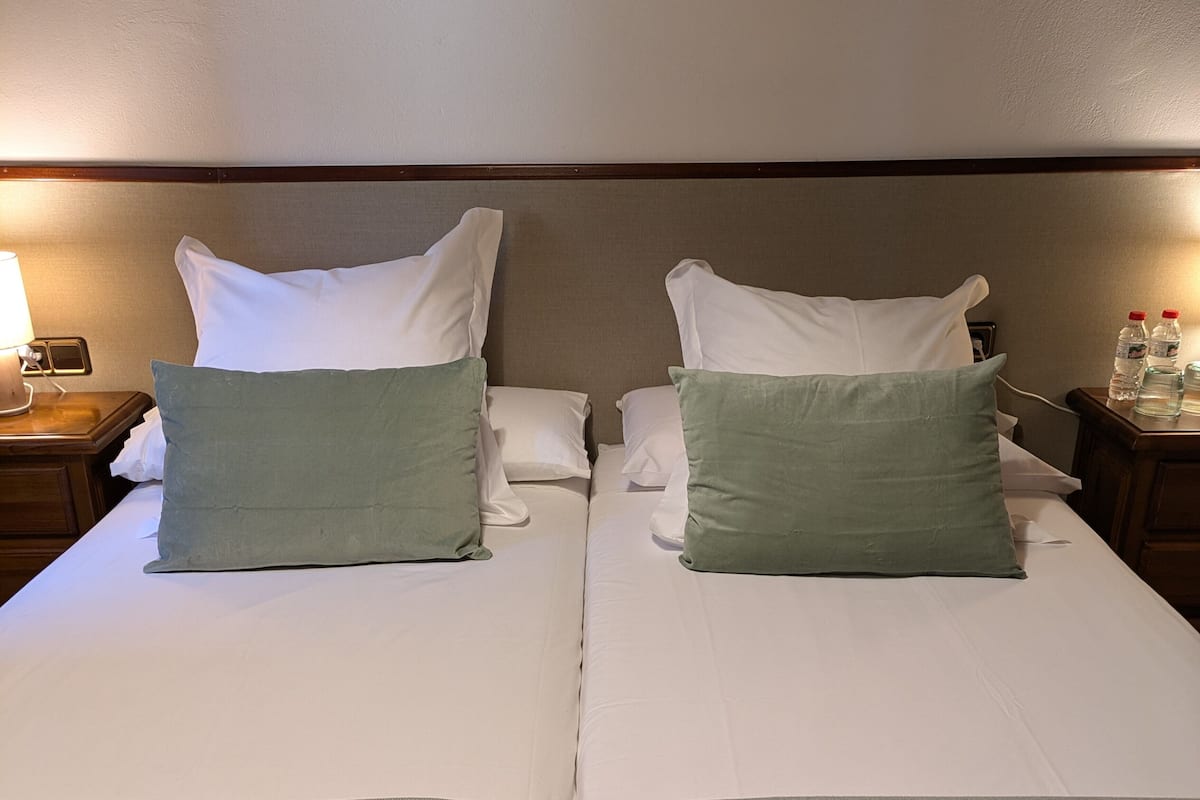 Un lit double avec deux oreillers, une table de chevet avec une lampe et une bouteille d’eau à proximité.