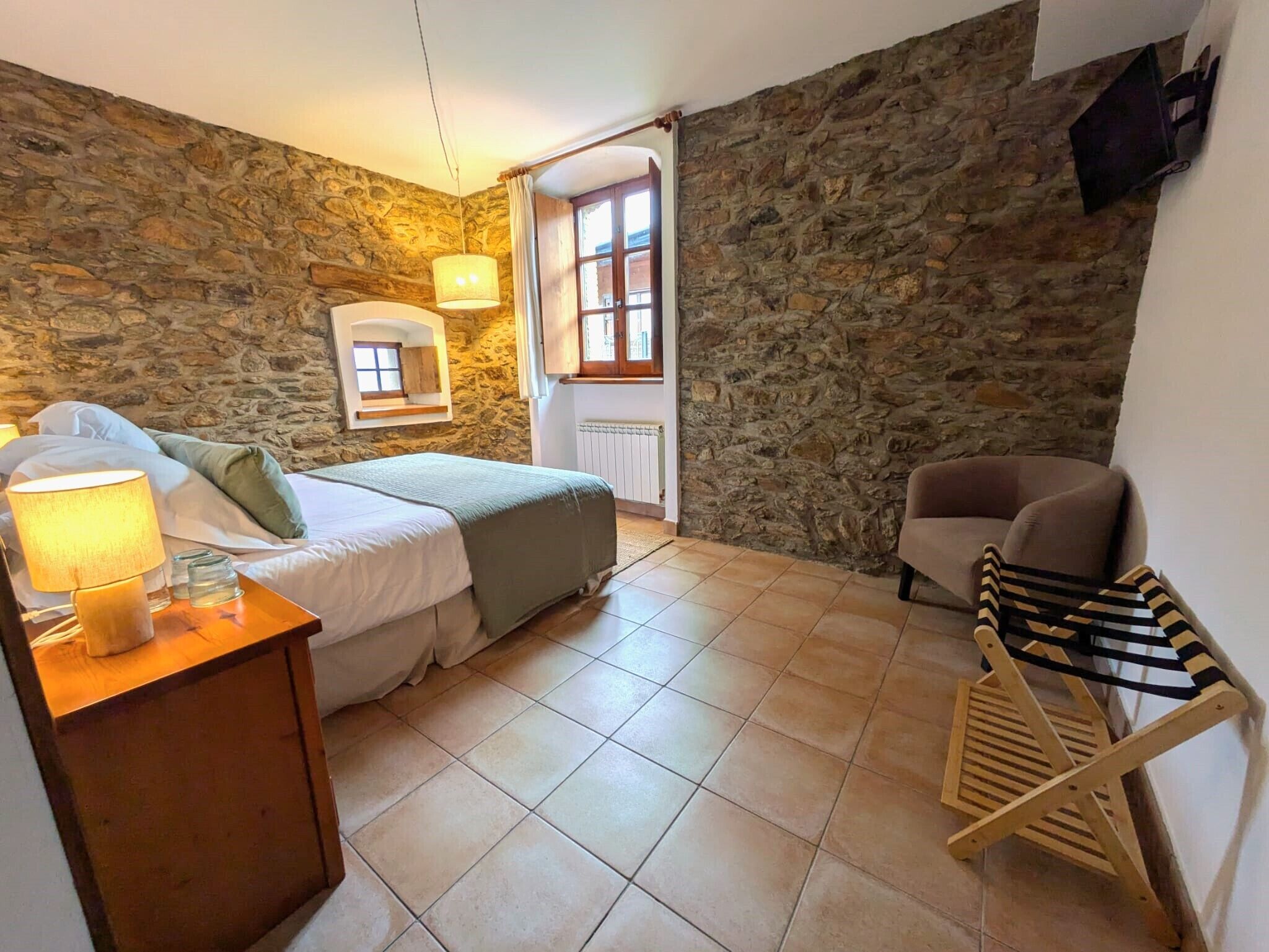 Une chambre avec un mur en pierre, un lit avec une table de chevet, une chaise et un étendoir en bois.