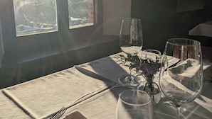 Una mesa de comedor con vistas al exterior a través de una ventana, un florero con flores y copas de vino vacías.