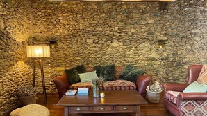 Una sala de estar acogedora con pared de piedra, una mesa de centro de madera, sofás de cuero y una lámpara de pie.