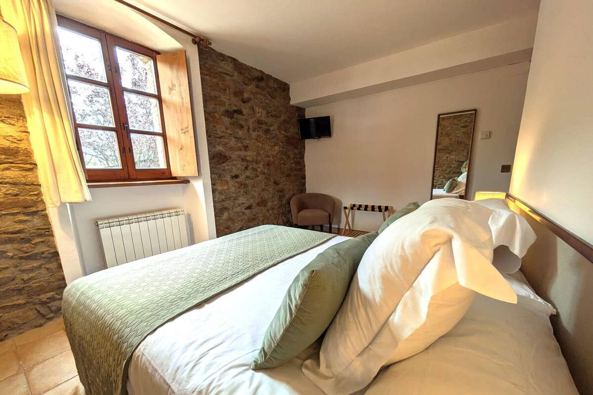 Une chambre à coucher comprenant un lit, une fenêtre, un mur en pierre, une chaise, une table et un téléviseur à écran plat.