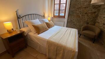 Una camera da letto con un letto, un comodino, una lampada, una sedia e una finestra vista alberi.