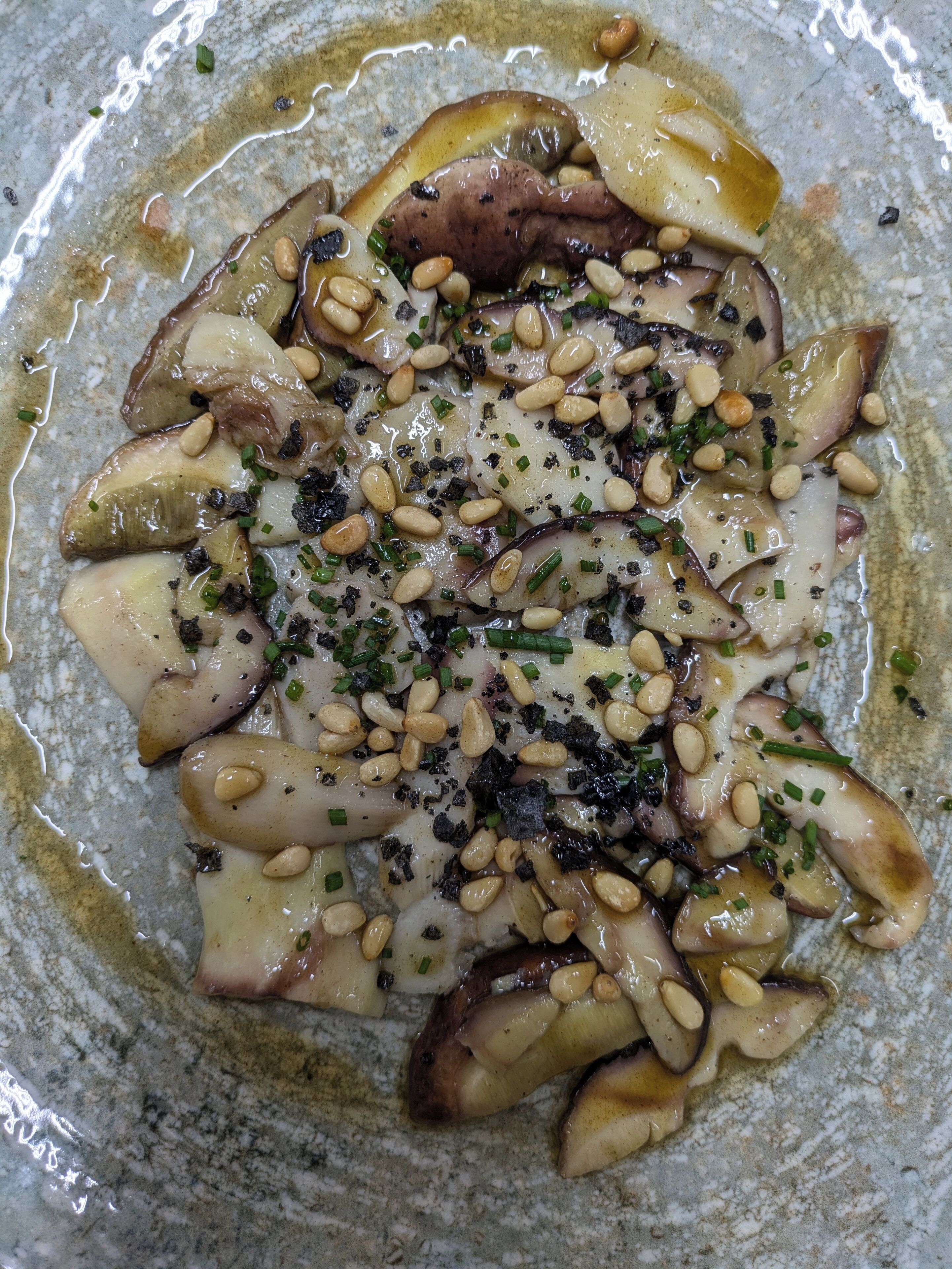 A close-up of a dish with octopus, pine nuts, and herbs.