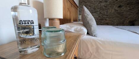Una mesita de noche de madera con una botella de agua, una lámpara y dos recipientes de vidrio.