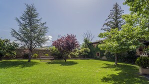 Un jardín bien cuidado con un banco, varios árboles y un muro de piedra.