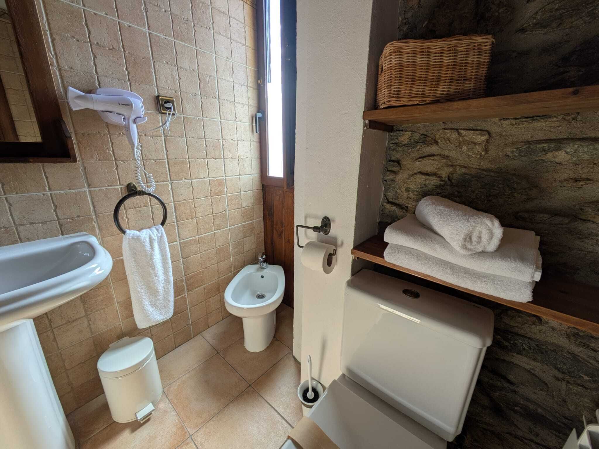 Bany compacte amb vàter, bidet i un petit rentapeus. Hi ha una tovallola penjada a la paret i una cistella a l'estant.