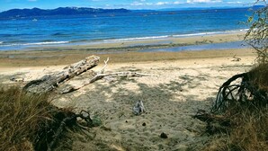 Une plage avec un ciel dégagé, une mer calme et des montagnes à l’horizon.