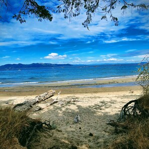 Ein Strand mit blauem Himmel, ruhiger See und fernen Bergen im Hintergrund.