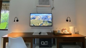 A room with a wooden desk, a white chair, a television, an air conditioner, and a small refrigerator. - Villa Peray Siargao (General Luna)