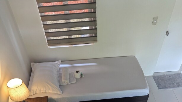 Two single beds with white linens, a bedside lamp, and a window with blinds.
