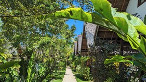 A pathway flanked by lush greenery and potted plants, leading to a building with a thatched roof. - Villa Peray Siargao (General Luna)