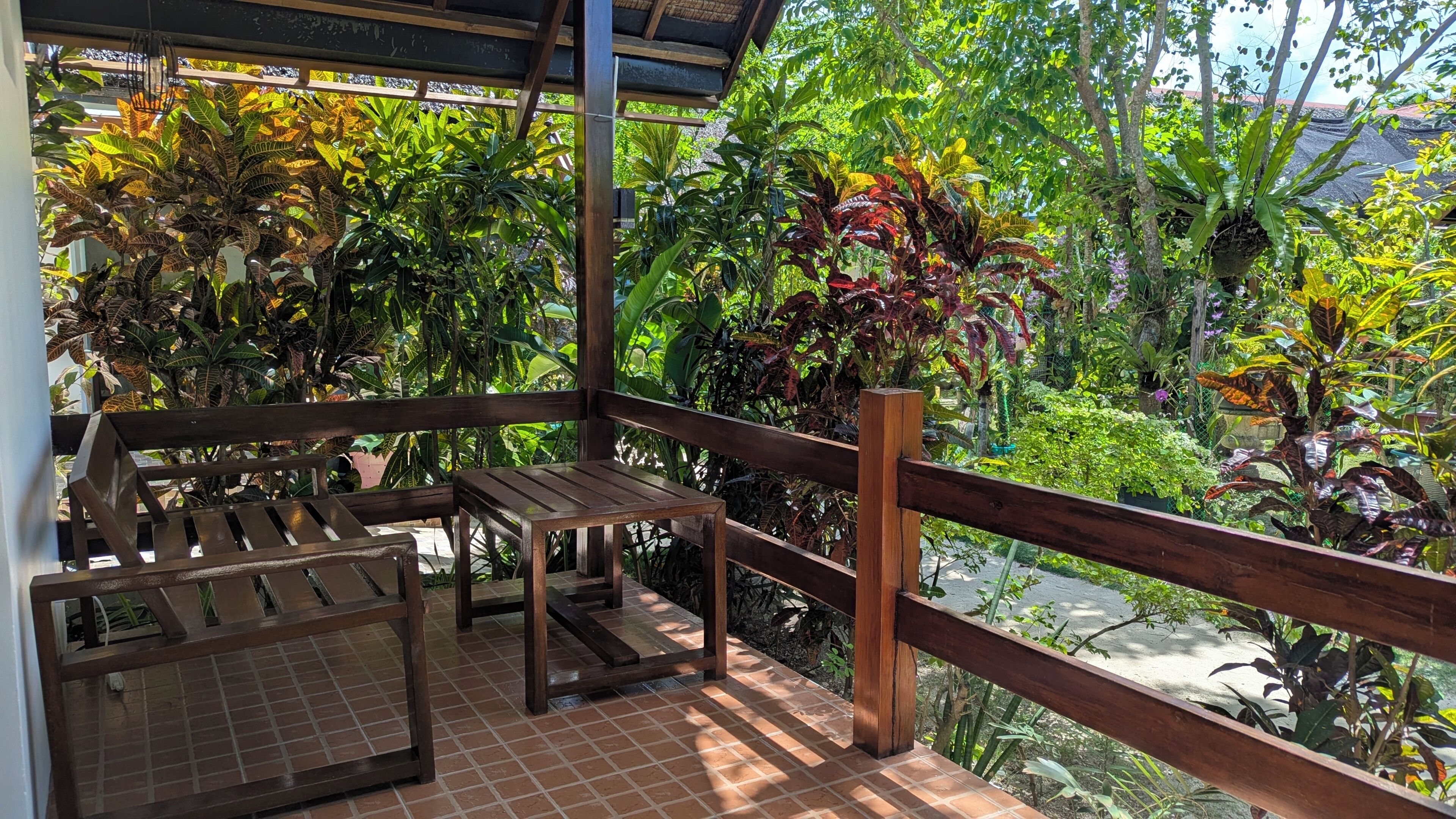 Un área de estar al aire libre, techada, con muebles de madera y vista a un follaje exuberante.