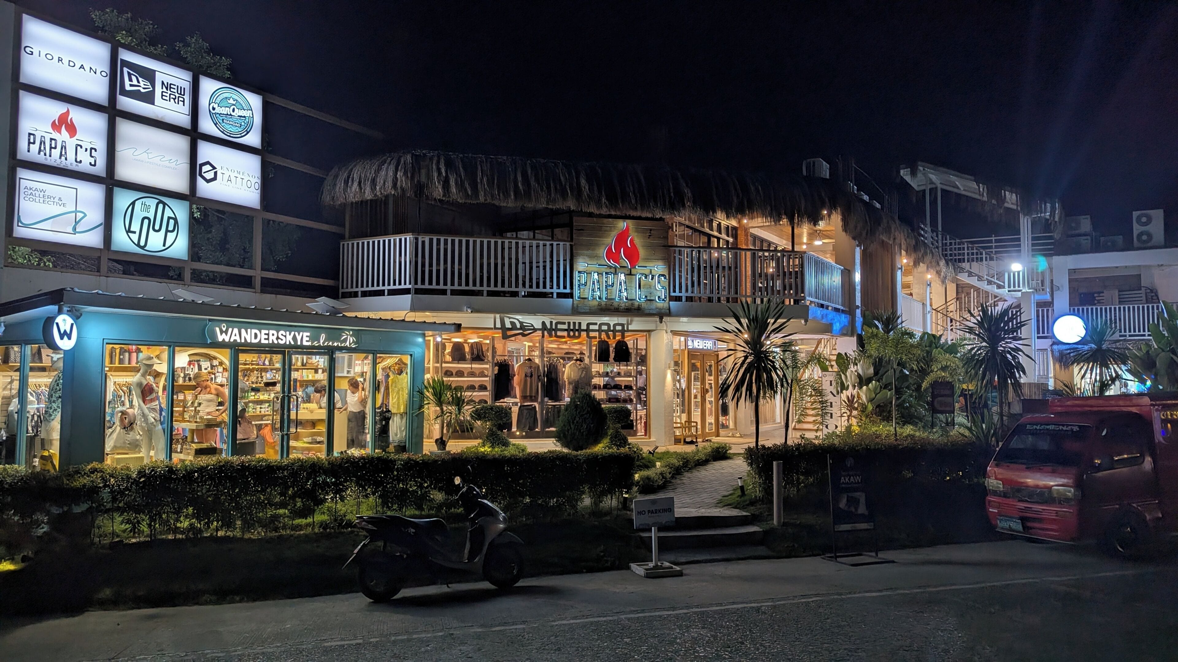 A building with multiple storefronts, including Papa C's, New Era, and others. There is a thatched-roof structure on the upper level.