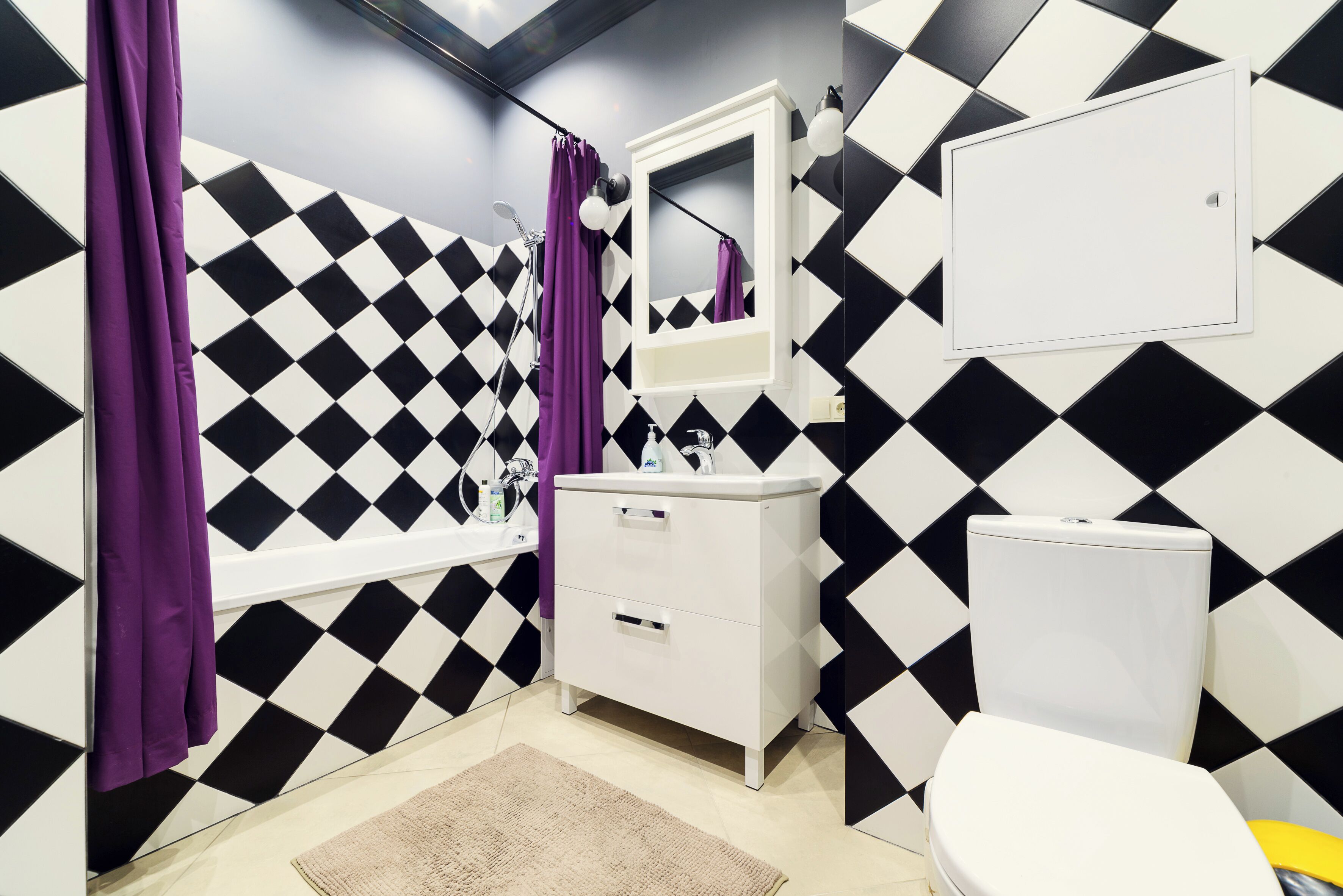 A bathroom with a black and white diamond-patterned wall, a white sink, a mirror, and a toilet.