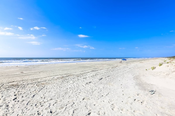 A beach with footprints and a blue umbrella.