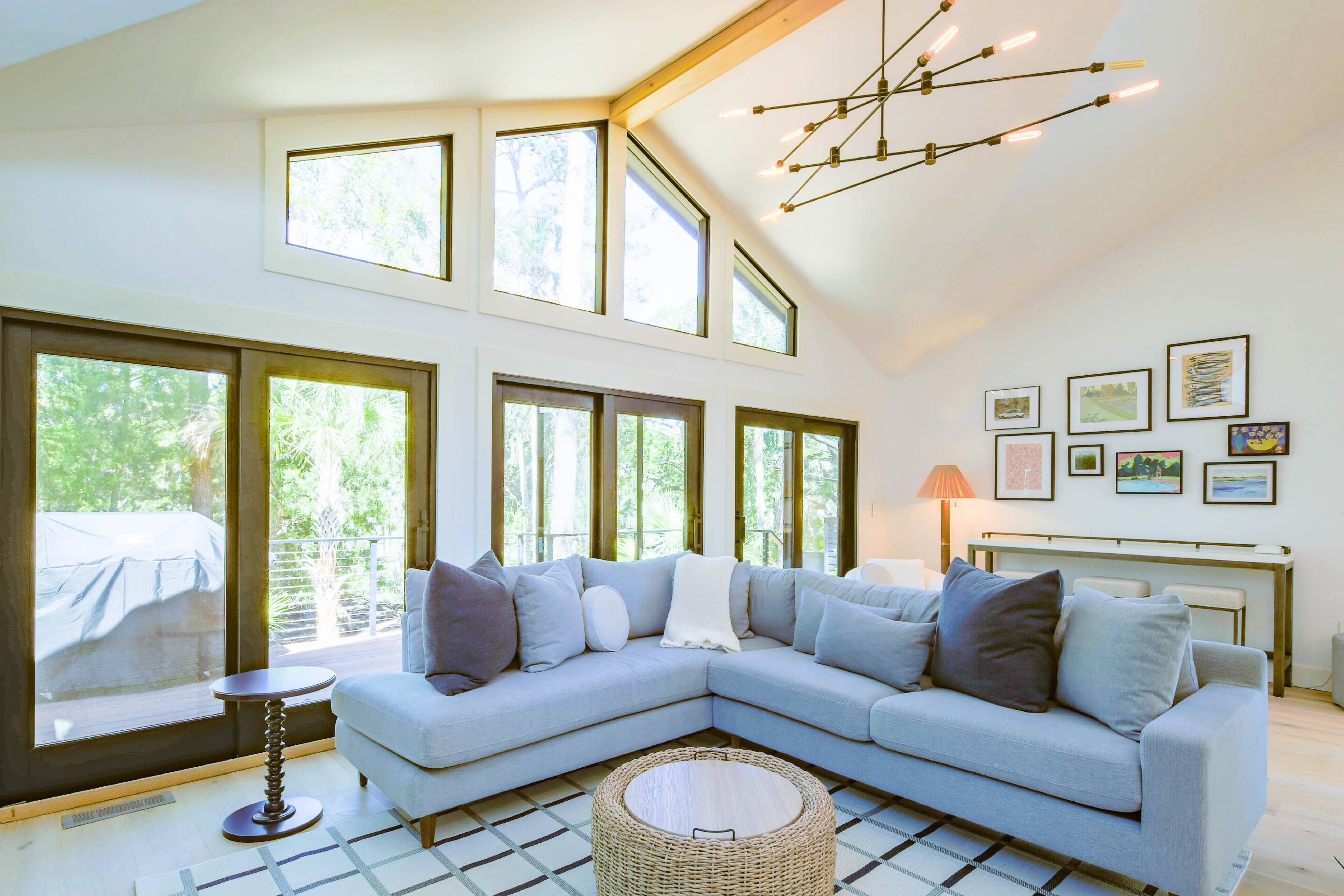 A modern living room with a light blue sectional sofa, large windows, and a ceiling light fixture.