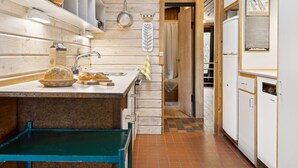 Cocina compacta con paredes de madera, un lavamanos, una pequeña zona de comedor y un refrigerador.