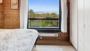 Un dormitorio con un ventanal grande, paredes de madera, una cama y un armario.